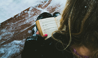 image of girl reading on a snowy bench